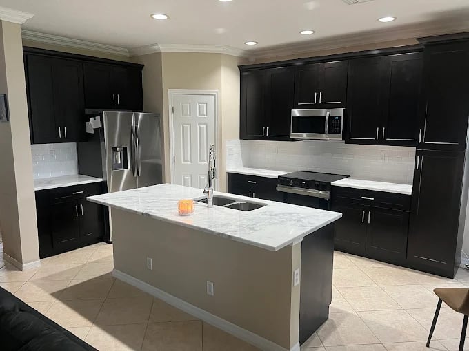 Modern kitchen with black cabinets, marble island, and stainless steel appliances