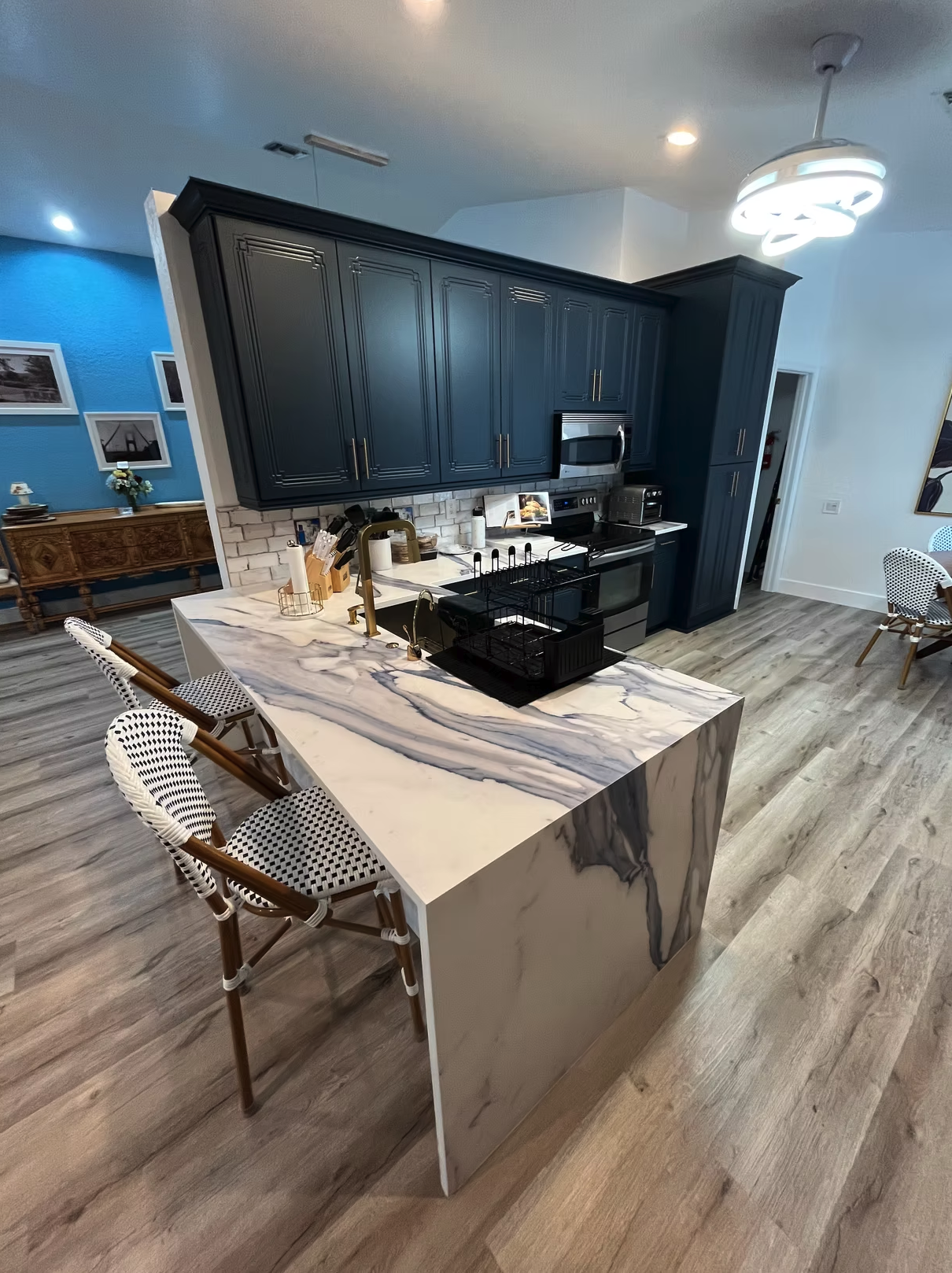 Modern kitchen with navy cabinets, marble countertop, and woven bistro chair