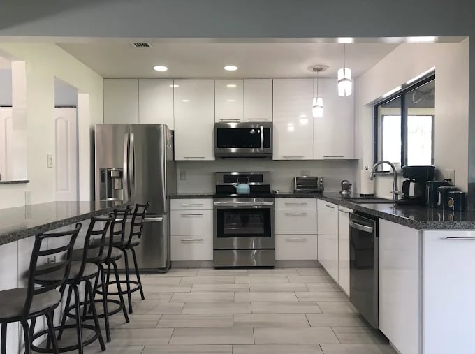Modern white kitchen with stainless steel appliances and black bar stools