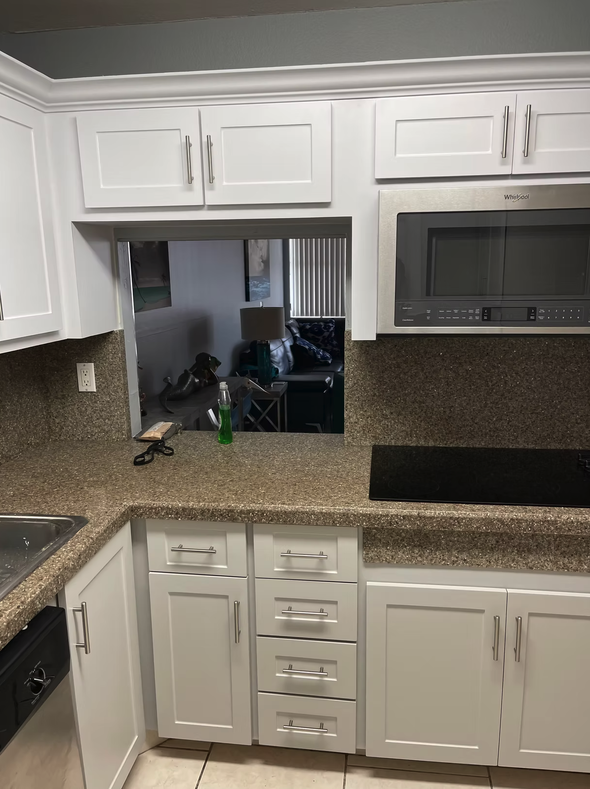White kitchen with granite countertops, microwave, and view into living room