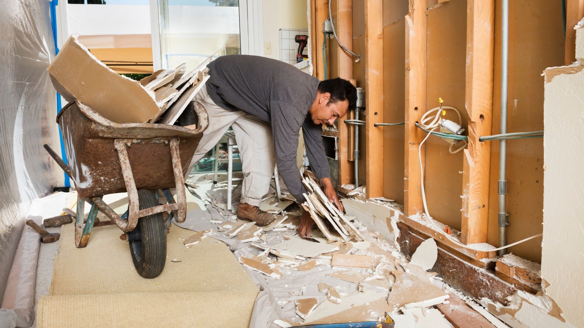 Worker cleaning up construction debris and broken materials near wheelbarrow