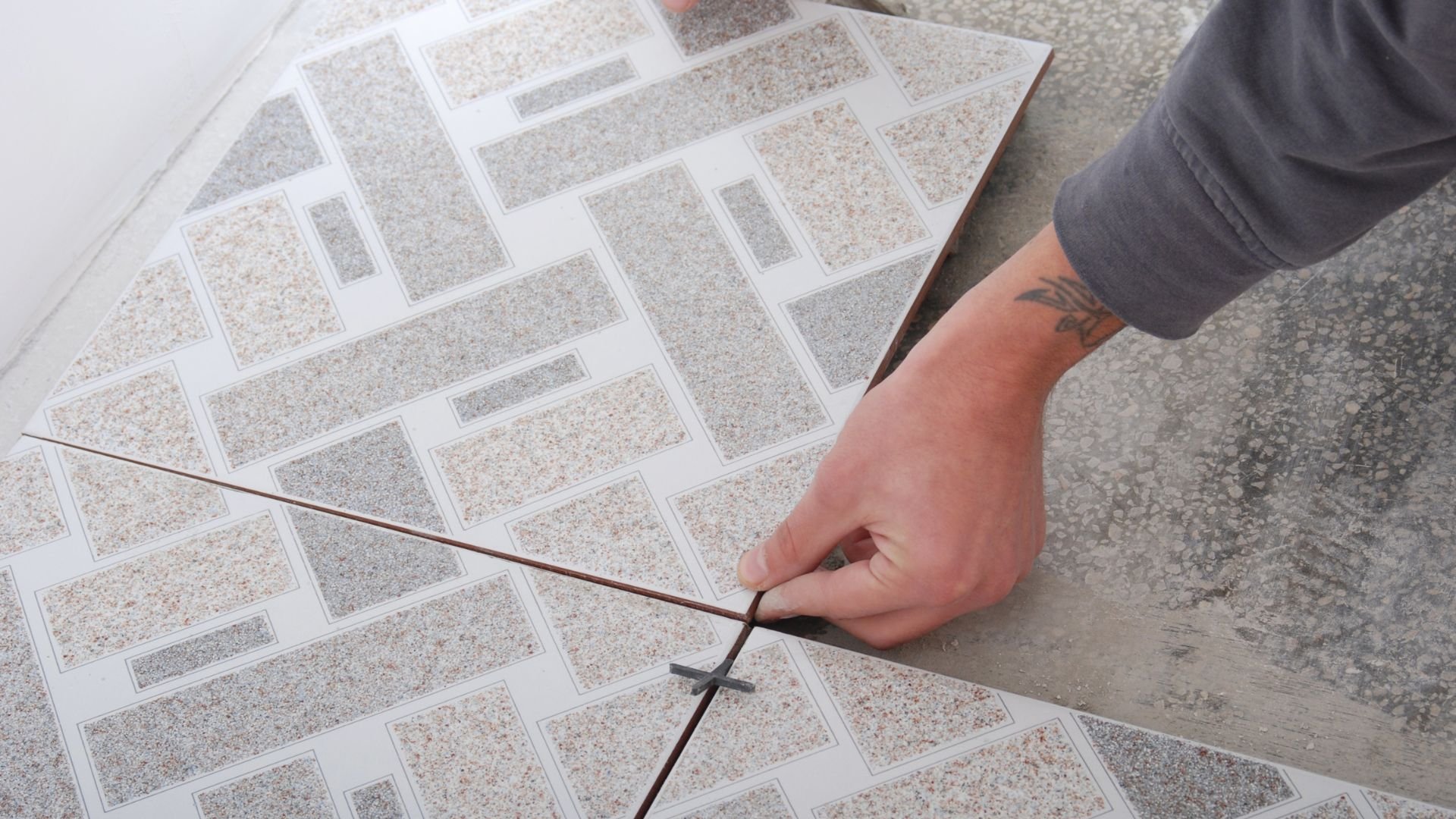 Hand placing tile spacer between light-colored ceramic floor tiles
